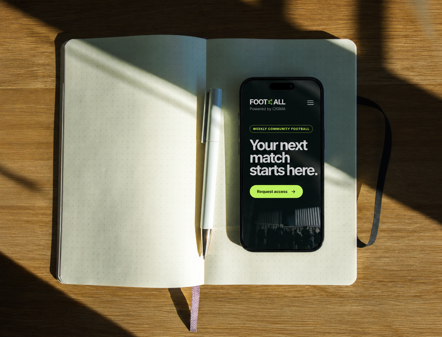 Phone showing the Football powered by CIGMA page beside a notebook.
